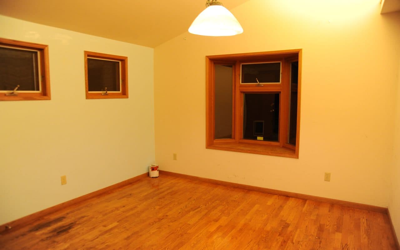 Empty dining room at night with two small windows on the left wall, a bay window ahead, a pendant light and a wood floor.
