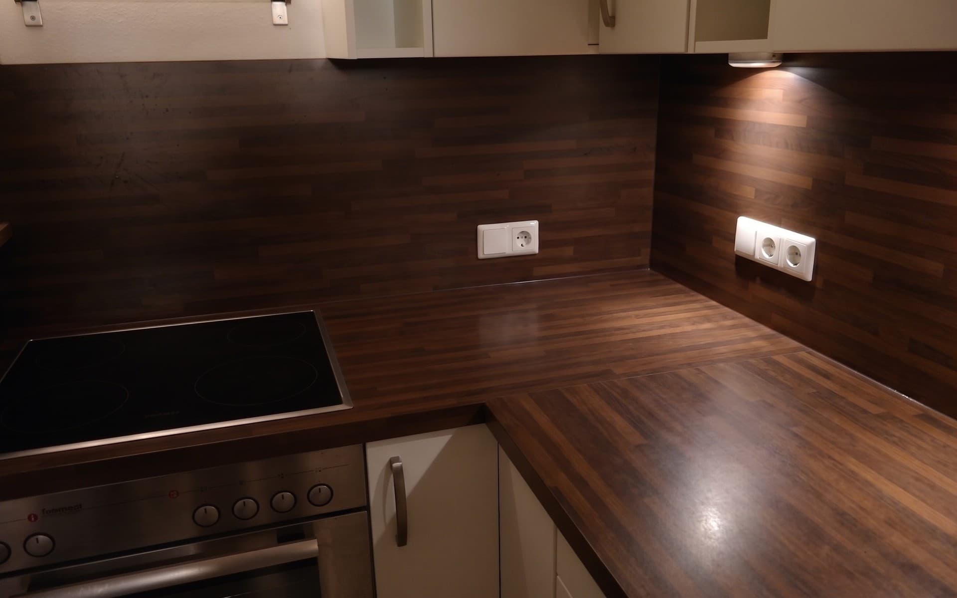 The same kitchen with the counters emptied by AI, showing a wood countertop, a cooktop, an oven and wall outlets.