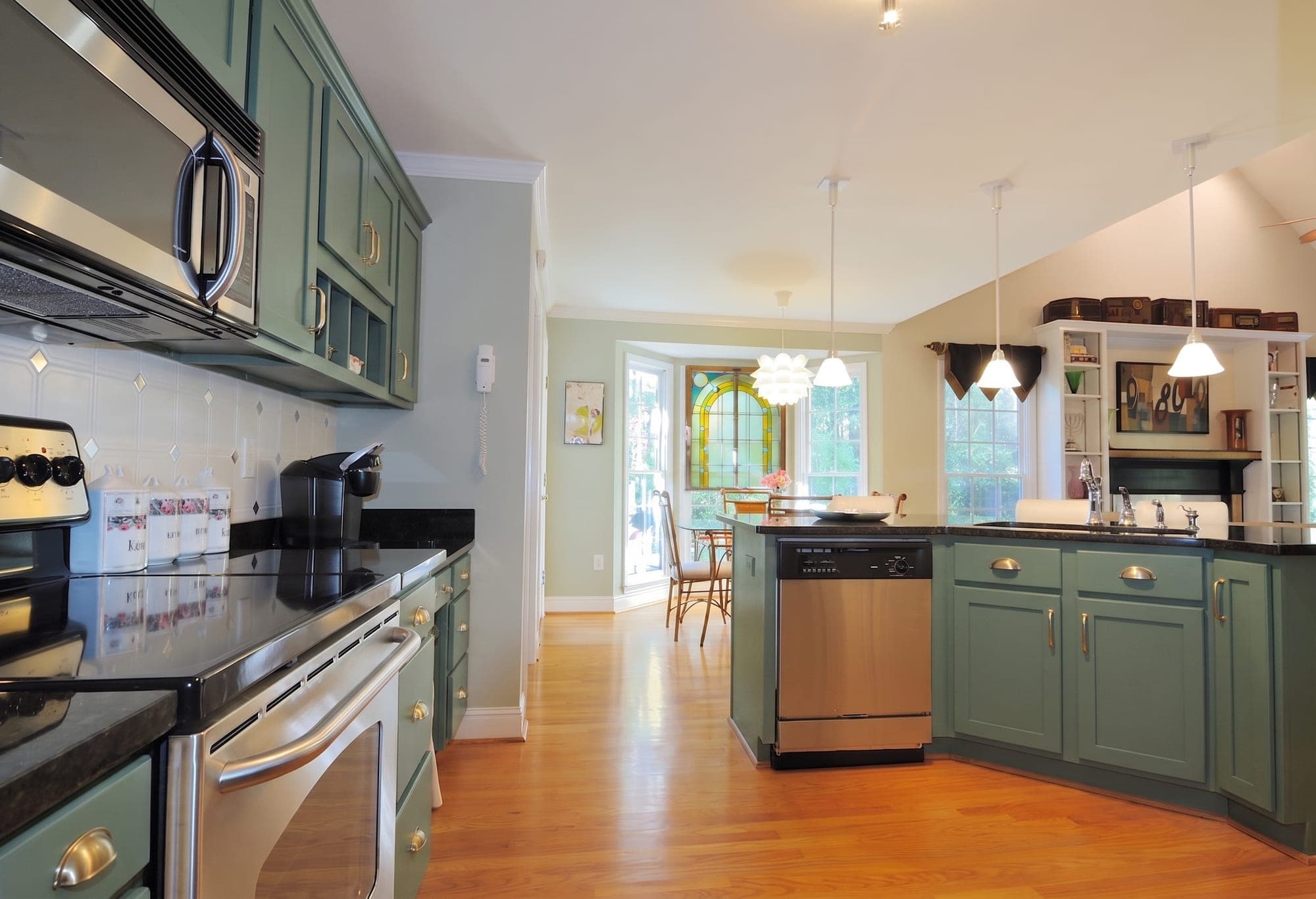 The same kitchen with the cabinets painted sage green and the counters, appliances, lights and floor unchanged.