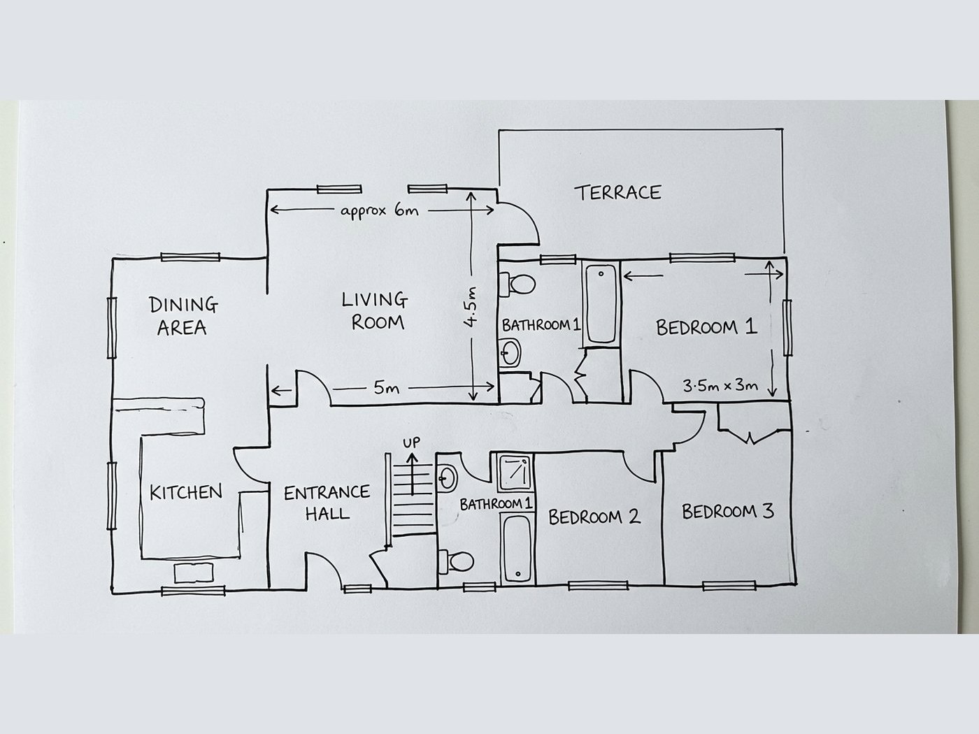 A floor plan drawn by hand on a sheet of paper and photographed, the paper edge and its shadow still in shot
